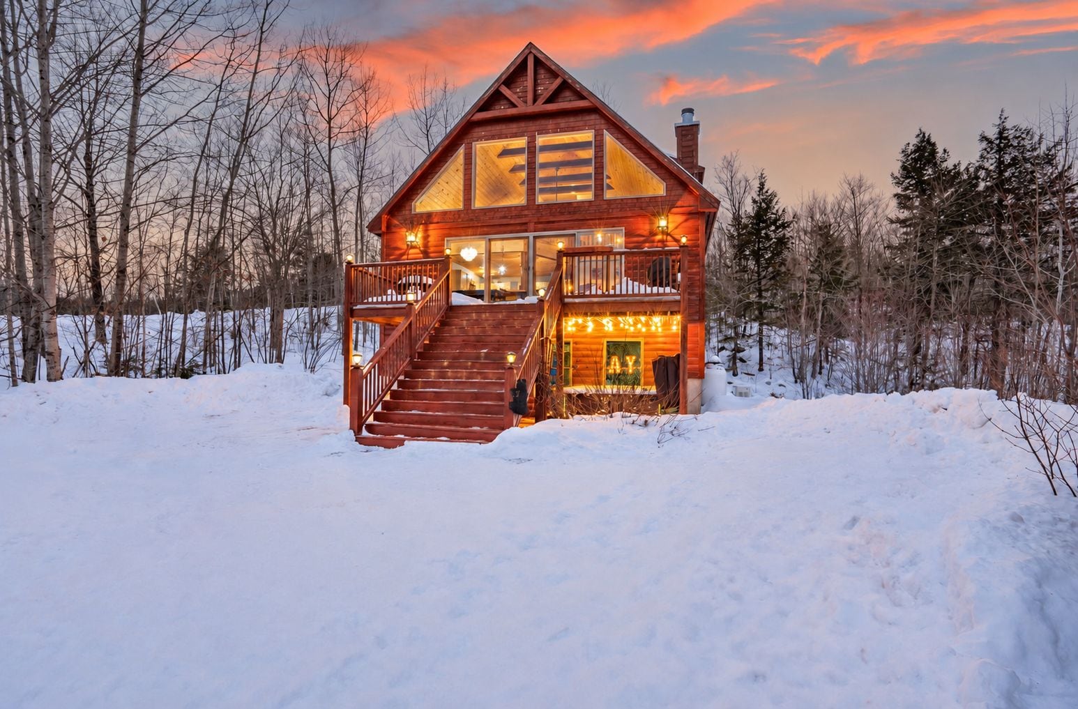 A log cabin with a staircase leading to a porch, surrounded by snow and trees.