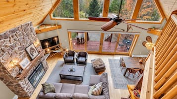 A cozy interior with a stone fireplace, a seating area with sofas and chairs, a dining table, and a view of the outdoors through large windows.