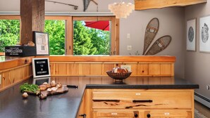 A wooden kitchen with a large island, a red umbrella, and a view of greenery outside. - Hot Tub, Sauna, Game Room, Fire Pit, BBQ, Karaoke, Dogs OK (Bethel)