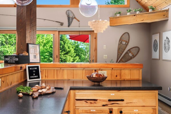 A wooden kitchen with a large island, a red umbrella, and a view of greenery outside. - Hot Tub, Sauna, Game Room, Fire Pit, BBQ, Karaoke, Dogs OK (Bethel)