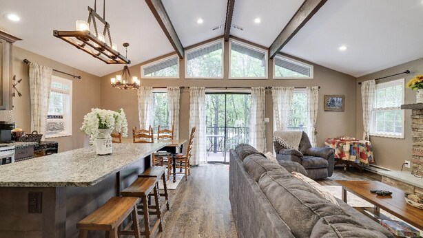 A spacious living area with a large gray sofa, a dining table with chairs, and a kitchen area with a granite countertop. - Peaceful Pocono Home Hot Tub minutes away from Kalahari, Camelback, Mt Airy (Long Pond)