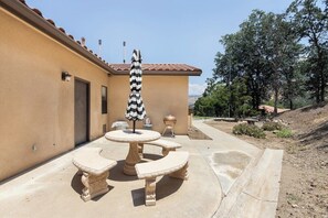 An outdoor patio with a round table, two benches, and a striped umbrella.