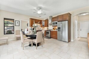 A modern kitchen with a dining area, featuring a central island, wooden cabinets, stainless steel appliances, and a ceiling fan.