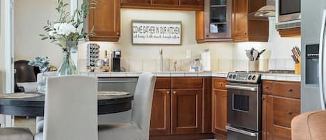 Una cocina con armarios de madera, una mesa de comedor con sillas, una estación de café y un reloj en la pared.