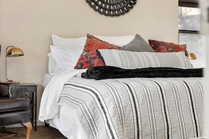A bed with multiple pillows and a striped blanket, a bedside lamp, and a chair.
