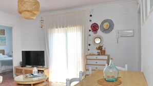 A living room with a TV, a wooden dining table, wicker furniture, and decorative items on the wall. - Apartment Virtudes III (Conil de la Frontera)