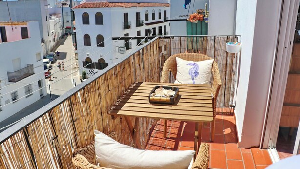 A balcony with wicker furniture, a table with a tray, and a view of the cityscape. - Apartment Virtudes III (Conil de la Frontera)
