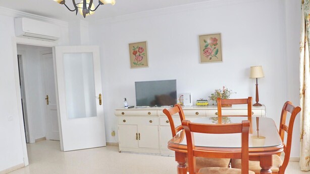 Un comedor con una mesa y sillas de madera, un televisor sobre un mueble, y dos obras de arte floral en la pared.