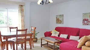 Sala de estar con un sofá rojo, una mesa de comedor de madera y sillas. Hay una planta en maceta y un cuadro en la pared.