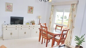 Una sala de estar con televisor, una mesa de comedor con sillas, un sofá, una lámpara y una planta en maceta.