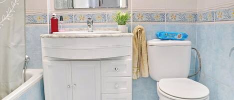 A bathroom with a white sink, mirror, and toilet. There is a towel hanging on the wall and a small potted plant on the sink.