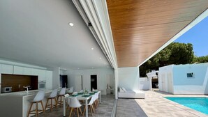 A modern kitchen with white cabinets and a dining area with a long table and chairs. - El Azul House in Chiclana (Chiclana)