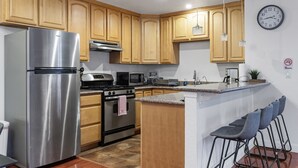 A modern kitchen with wooden cabinets, stainless steel appliances, a microwave, and a clock on the wall. - Convenient Modern COZY 4BA/2BR Hidden GEM (Milpitas)