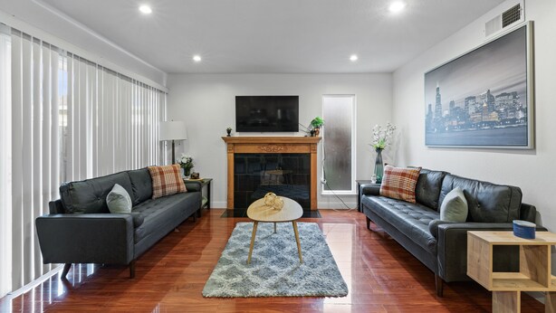 A modern living room with two sofas, a fireplace, and a cityscape painting. - Convenient Modern COZY 4BA/2BR Hidden GEM (Milpitas)