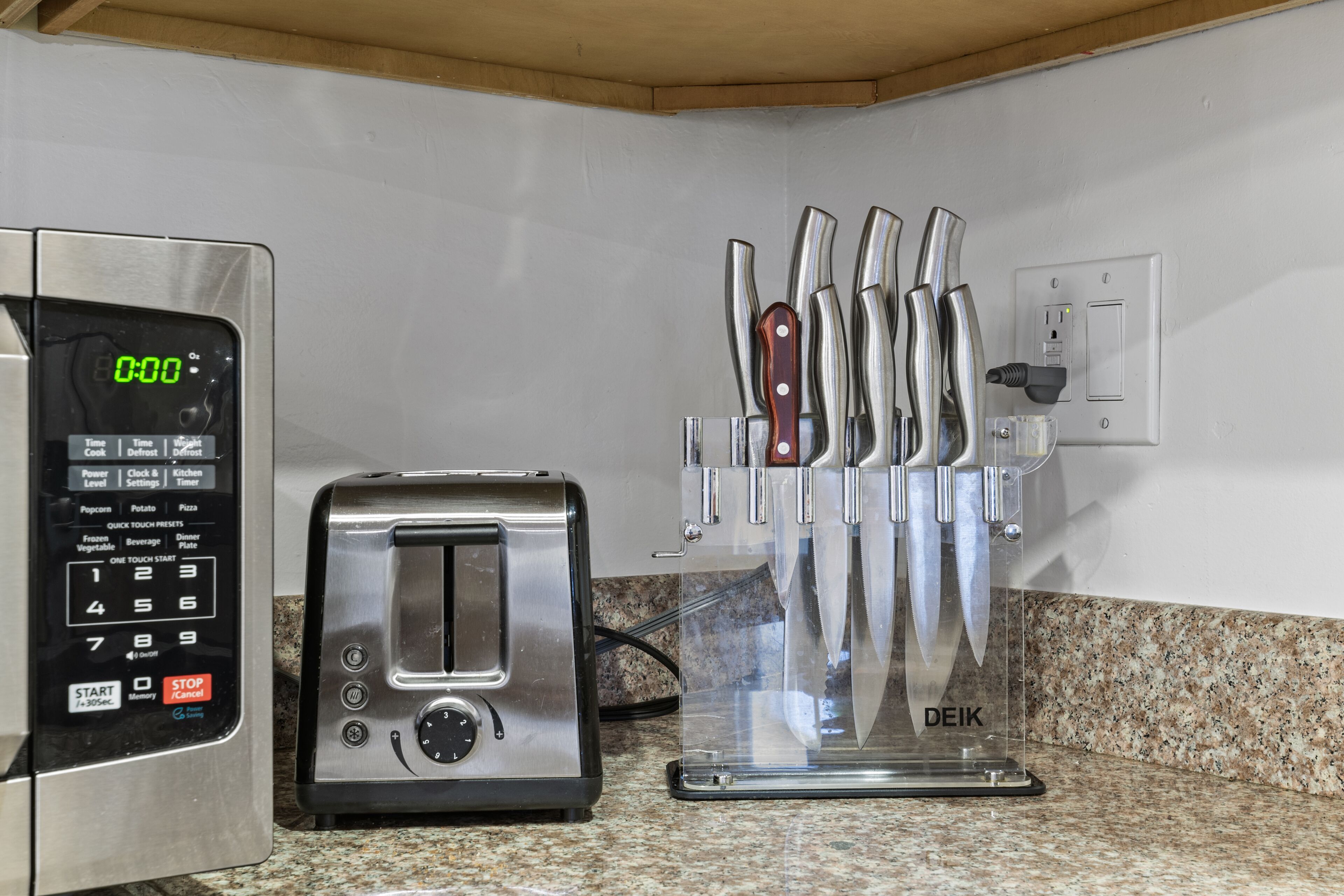 A kitchen with a digital clock, a toaster, and a knife block.
