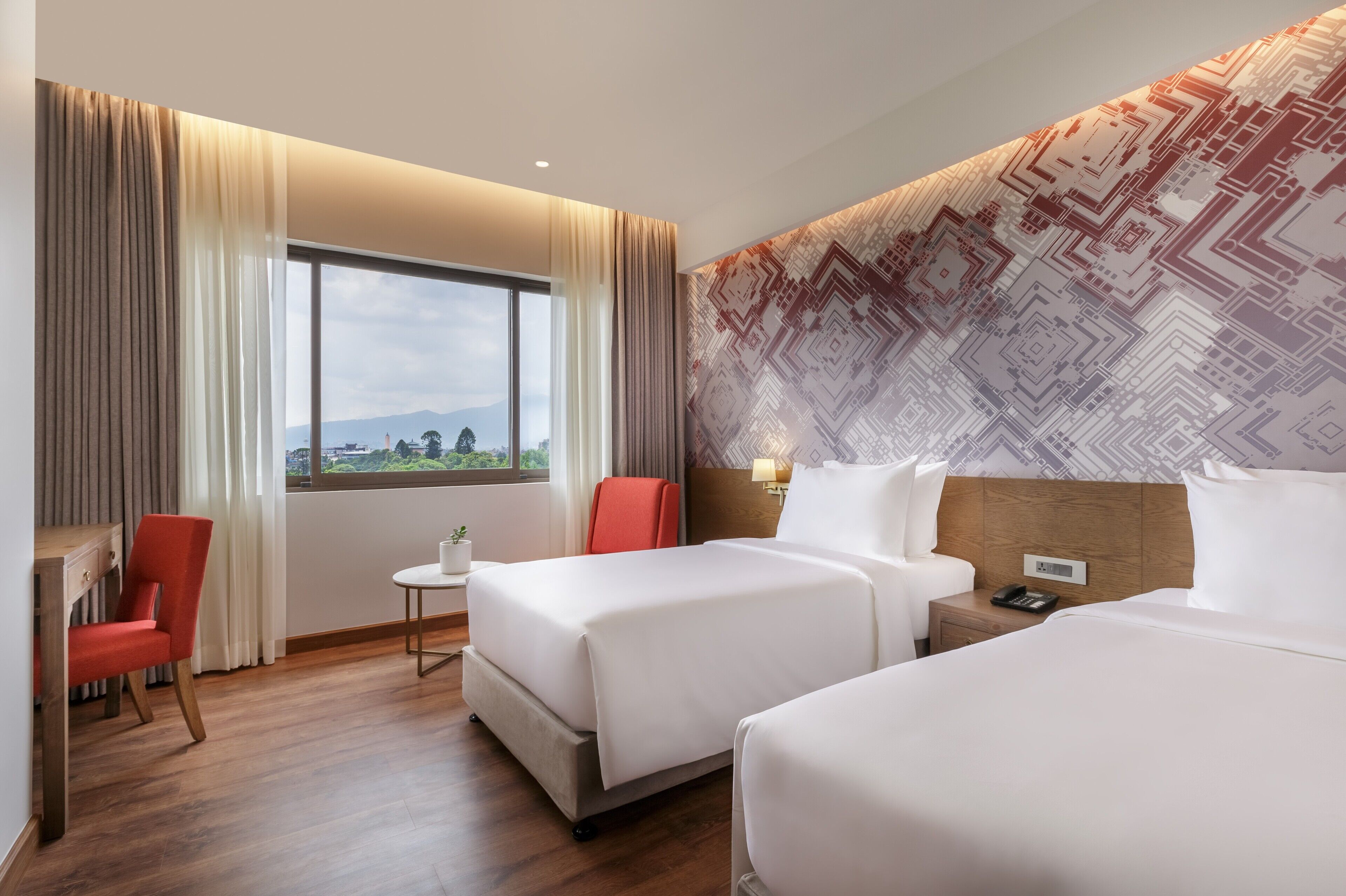 A hotel room with two beds, a desk, a chair, a small table, and a window with curtains.