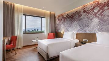 A hotel room with two beds, a desk, a chair, a small table, and a window with curtains.