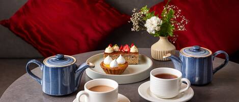 Une table dressée avec une théière, des tasses, des soucoupes, une théière, une assiette avec un gâteau et un vase rempli de fleurs.