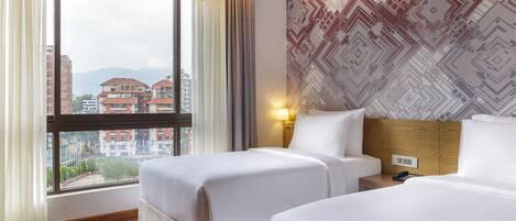 A hotel room with two beds, a large window with curtains, a patterned wall, and a nightstand with a lamp.