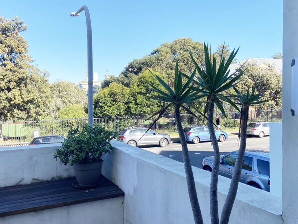 A balcony with a potted plant, a street view with cars, and a clear blue sky.