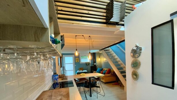 A modern kitchen with a wooden countertop, a dining area with a table and chairs, and a staircase leading to an upper level.