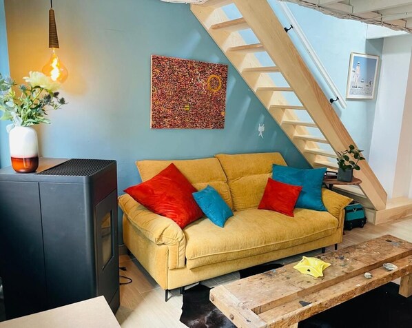 A living room with a sofa, a wooden coffee table, a radiator, a staircase, and a painting on the wall.