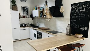 A modern kitchen with a wooden table, bar stools, a blackboard with recipes, and a washing machine.