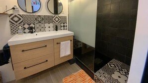 A modern bathroom with a white vanity, two wall-mounted mirrors, a shower with black tiles, and patterned floor tiles.
