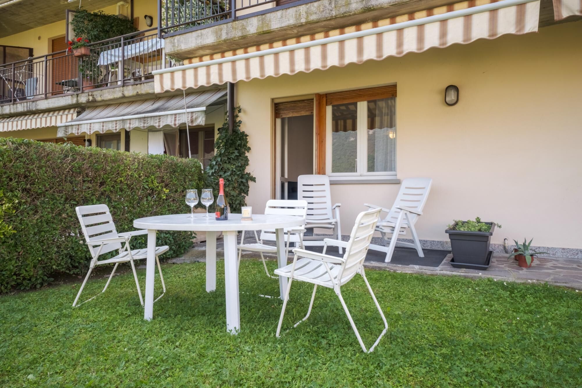 A patio with a round table, four white chairs, and a bottle of wine.
