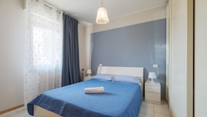Een slaapkamer met een bed, nachtkastje, lamp en plafondverlichting.