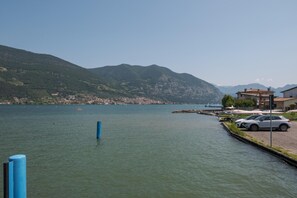 A lakeside view with a dock, a white car, and a building with a red roof. - Interno 2 in Iseo With 1 Bedrooms and 1 Bathrooms (Iseo)