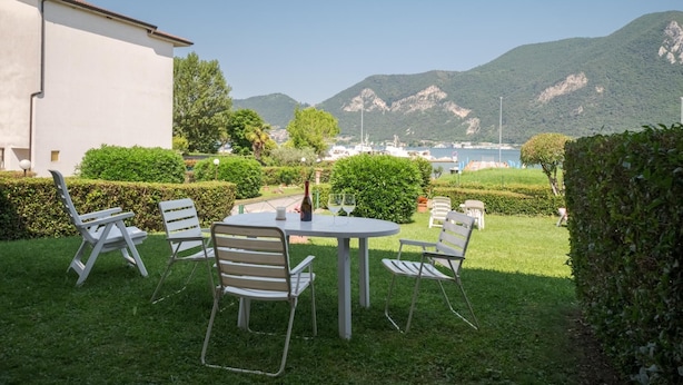 Een terras buiten met een ronde tafel en stoelen, omringd door keurig onderhouden hagen en uitzicht op een bergachtig landschap.