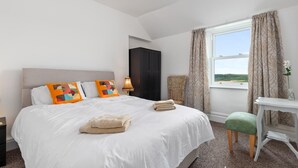 A bedroom with a large bed, a nightstand, a desk, and a chair. There is a window with curtains and a view of the outdoors.