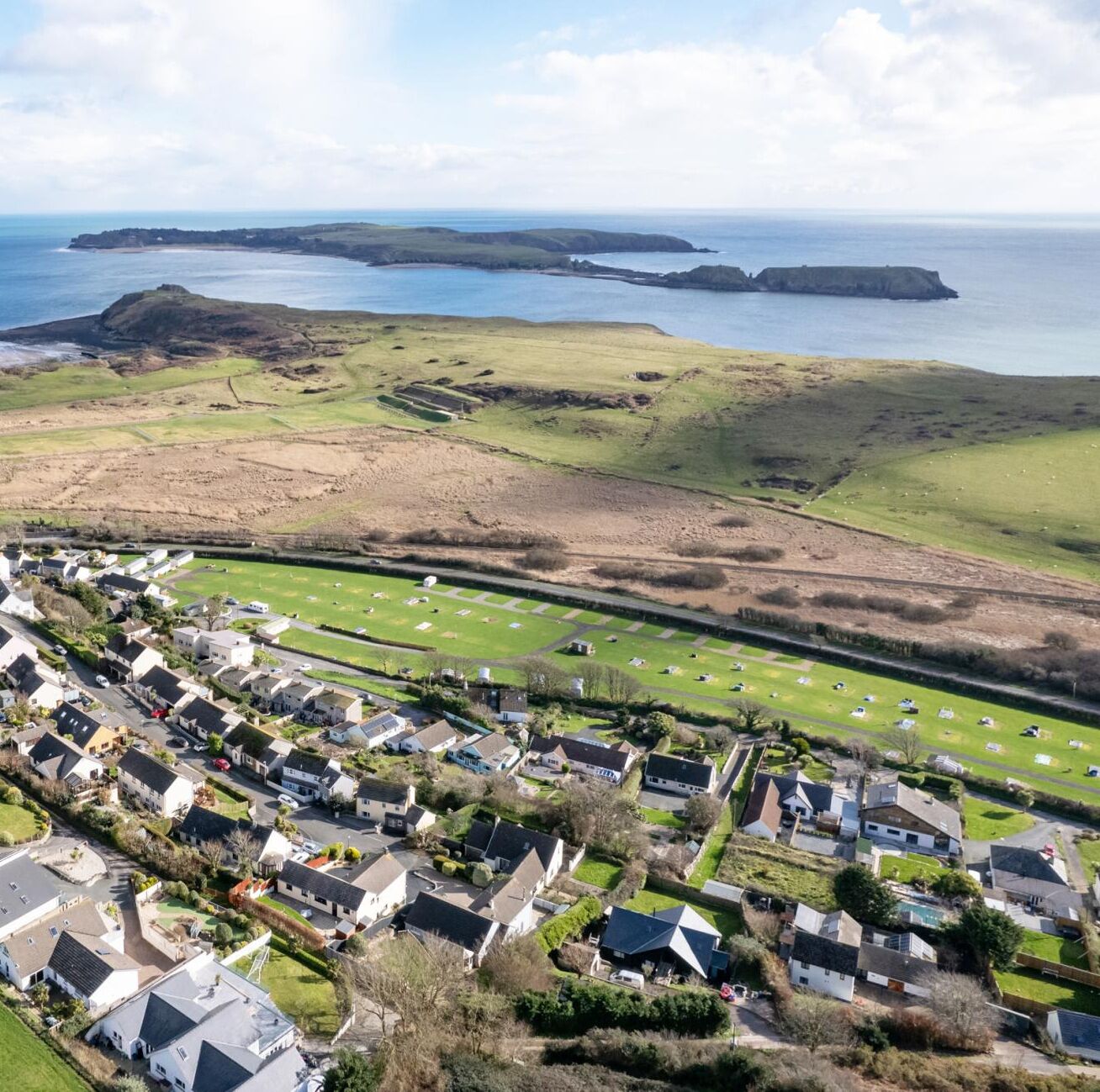 A coastal residential area with houses, a road, and a grassy field.