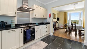 A modern kitchen with white cabinetry, a stainless steel range hood, and a black countertop.