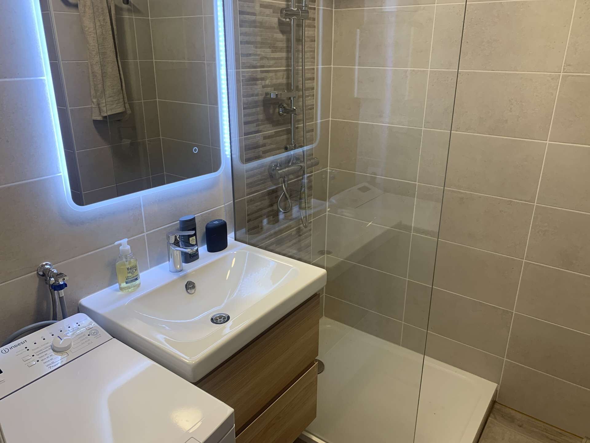 Une salle de bain moderne avec un lavabo blanc, un miroir et une cabine de douche en verre.