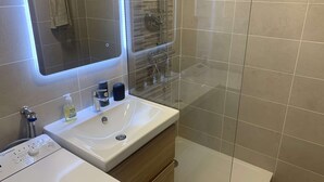 A modern bathroom with a white sink, a mirror, and a glass shower enclosure. - Renovated studio, sea view, close to beaches and shops... (ST MANDRIER SUR MER)