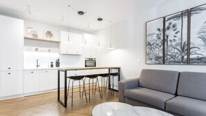 Une cuisine moderne avec des meubles blancs, un coin repas doté d’une table en marbre et un canapé gris.