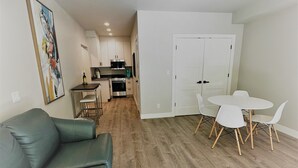 A modern living room with a green sofa, a dining area with white chairs, and a kitchen in the background. - Outlaw Inn Unit 1. Air conditioning, newly remodeled. Steps from Main Street! (Ouray)