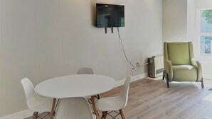 A modern living room with a round white table, white chairs, a mounted flat-screen TV, a green armchair, and a large window. - Outlaw Inn Unit 1. Air conditioning, newly remodeled. Steps from Main Street! (Ouray)