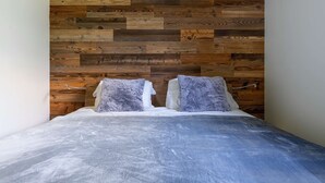 Ein Bett mit grauer Bettdecke, zwei Kissen und einem Holzkopfende mit Fischgrätmuster.