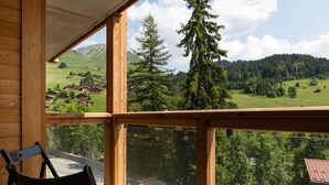 Eine Holzhütte mit einem Balkon, der einen Blick auf ein grünes Tal mit Häusern und Bäumen bietet.