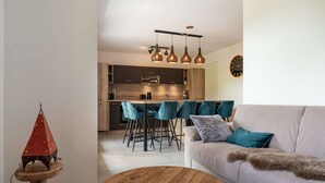 Ein modernes Wohnzimmer mit Sofa, Couchtisch und Essbereich mit Stühlen, im Hintergrund eine Küche.