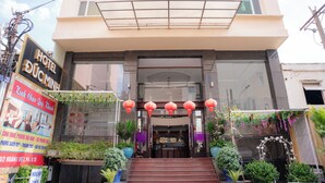 L’entrée d’un hôtel, avec une enseigne, des marches menant à l’entrée et des plantes en pot disposées autour.