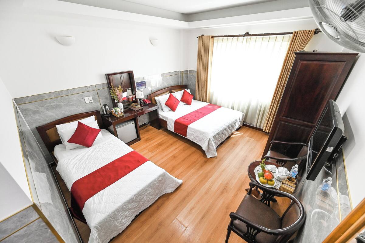 Une chambre d’hôtel avec deux lits, un bureau avec une chaise, une petite table avec un panier de fruits et une télévision.