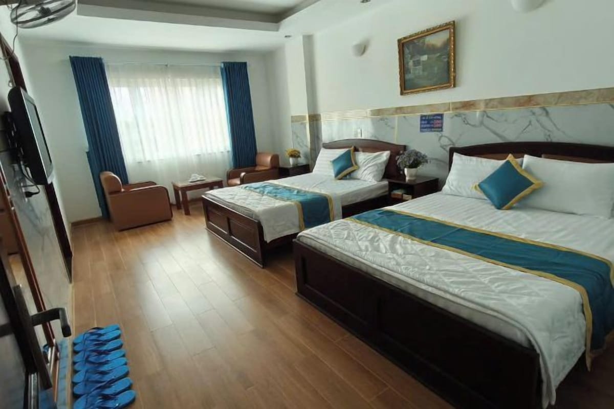 Une chambre d’hôtel avec deux lits, un bureau, une chaise et une grande fenêtre avec des rideaux.