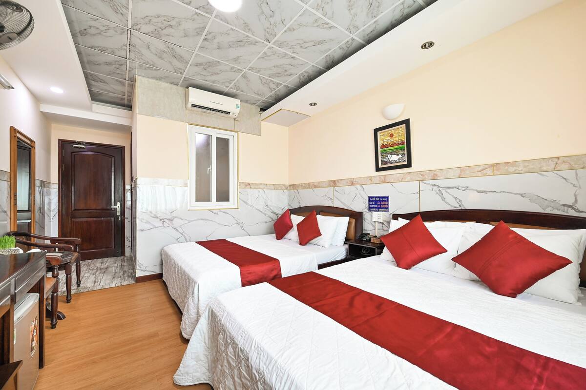 Une chambre d’hôtel avec deux lits, un bureau en bois, une fenêtre et un plafond en marbre.