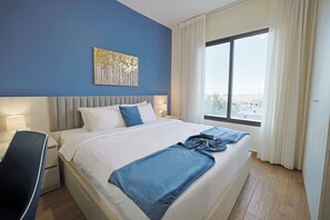 A hotel room with a large bed, a desk, and a window with curtains. - 46 Serviced Apartments (Amman)