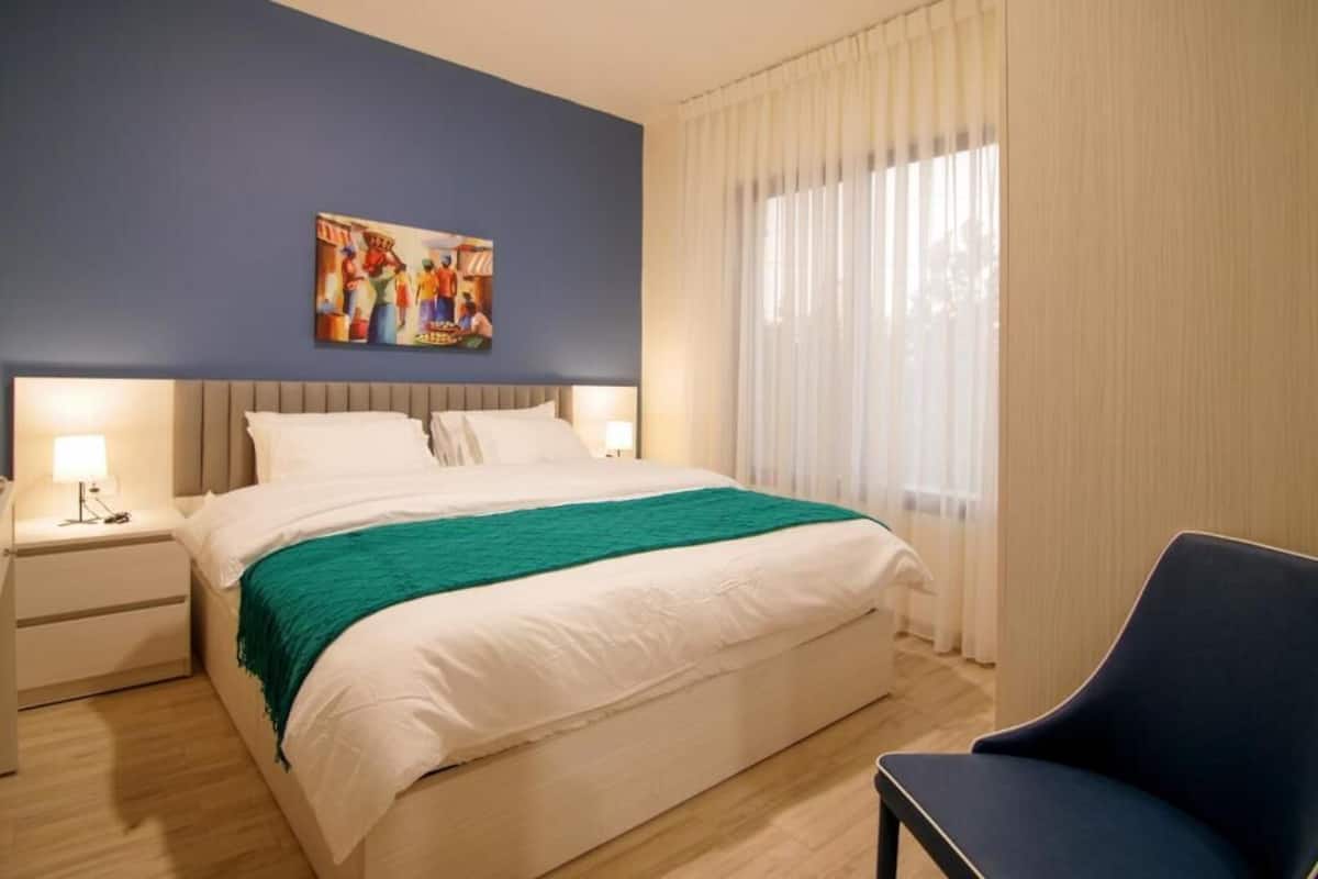 A hotel room with a bed, a nightstand, a chair, a painting on the wall, and a window with curtains.