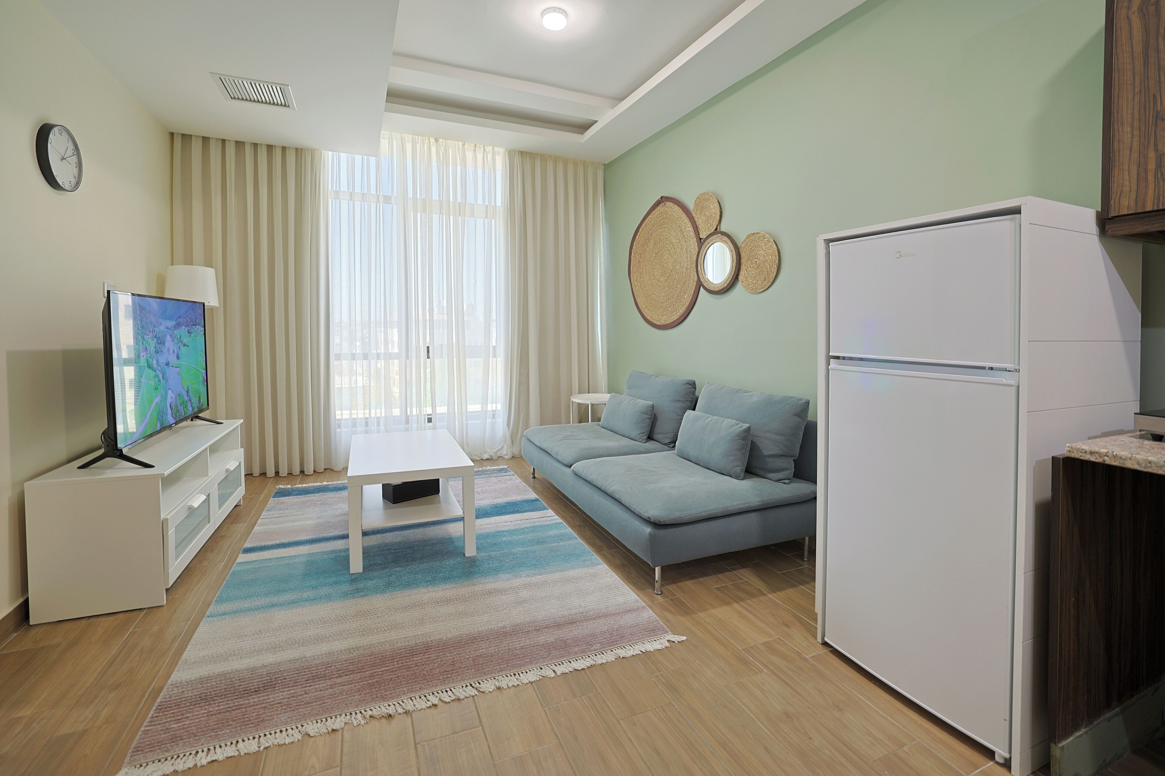 Uma sala de estar moderna com sofá, mesa de centro, televisão de tela plana, geladeira e área de jantar.